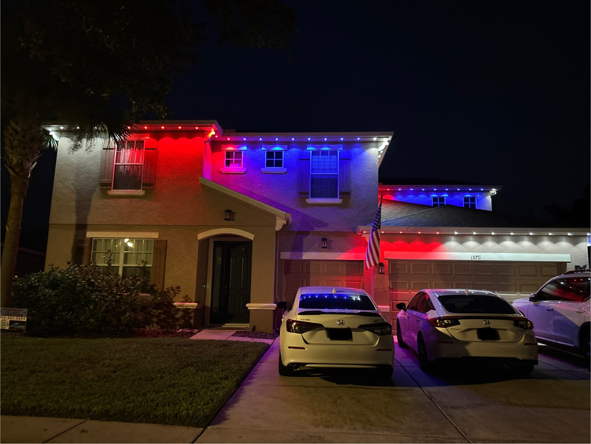 Two-story home glowing in red, white, and blue permanent holiday lighting