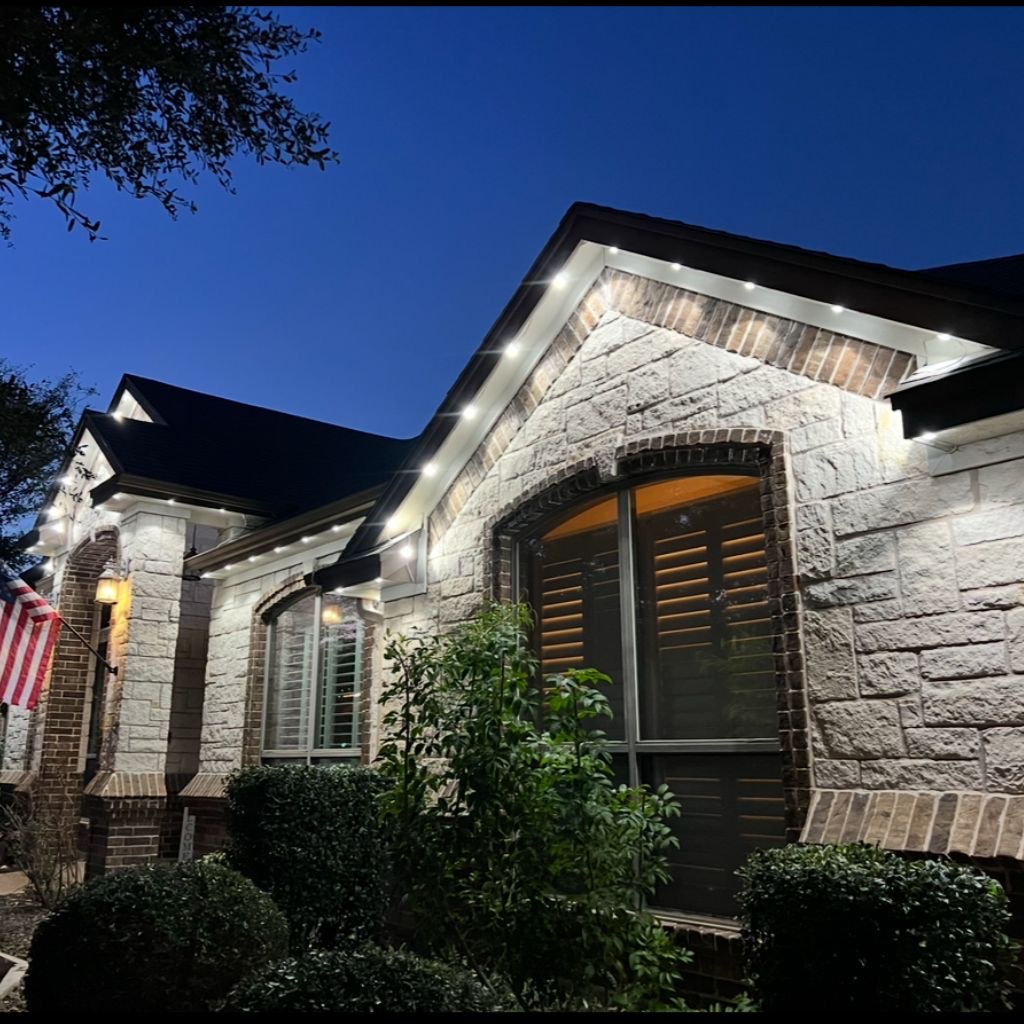 Stone home with warm white roofline lighting against a twilight sky